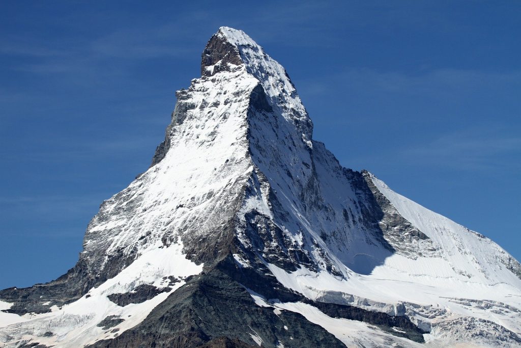 A snow-covered mountain peak, spelled P-E-A-K, against a bright blue sky